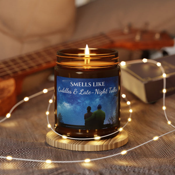 Candle in a jar with a label featuring two people and text, surrounded by string lights and a guitar in the background.