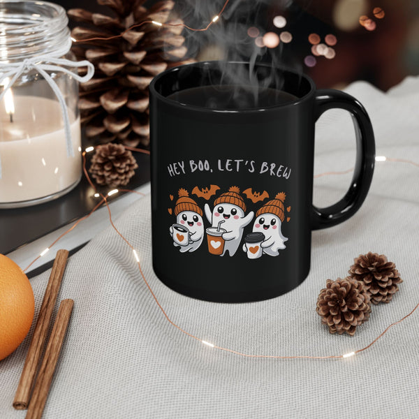 Black mug with Halloween-themed design featuring ghosts and text 'Hey Boo, Let's Brew' on a table with decorative items.