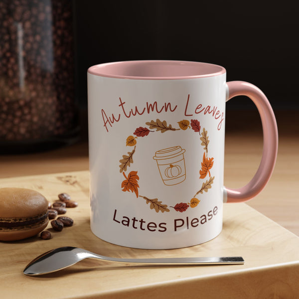 Mug with 'Autumn Leaves Lattes Please' text and autumn-themed design on a wooden surface with coffee beans and a spoon.