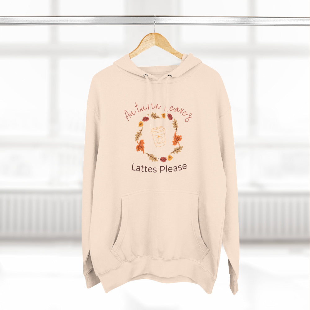 Beige hoodie with autumn leaves and lattes text on a hanger against a white background