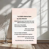 A personalized children's wall print with a soft blush pink background and black text, displayed in a styled room setting with a glass vase of dried stems on a wooden floor.