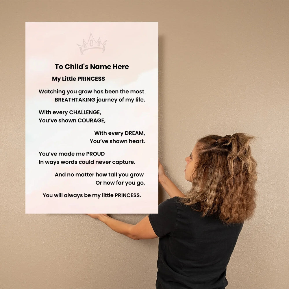 A woman in a black shirt holds a large personalized wall art print against a beige wall. The print has a white background with a faint pink crown at the top and a printed poem titled 'My Little PRINCESS' addressed to a child's name.