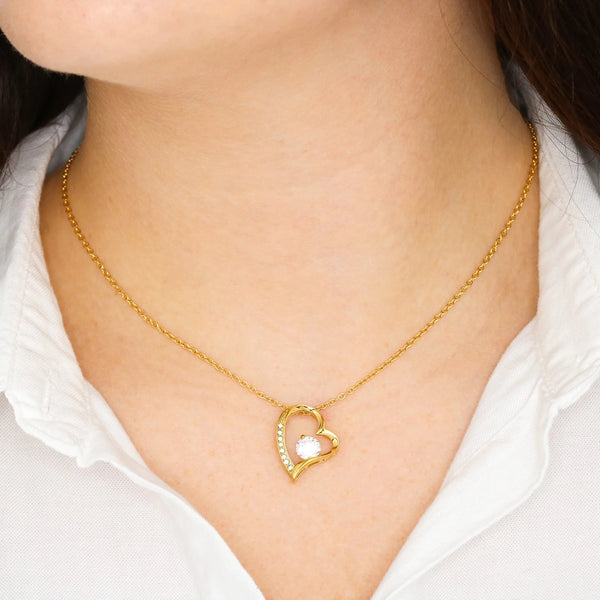 Gold heart-shaped necklace with a white stone on a person wearing a white shirt.