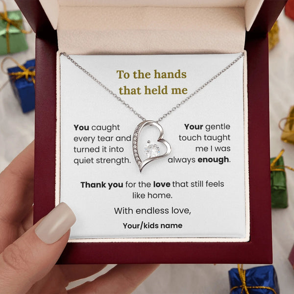 Heart-shaped necklace in a box with a sentimental message, held by a hand.
