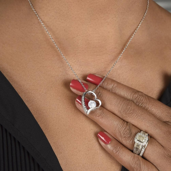 Heart-shaped silver necklace with a diamond pendant on a person wearing a black top.