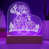 Personalized acrylic LED night light on a wooden base, featuring laser-engraved deer, trees, and romantic text, glowing with purple light in a room setting.
