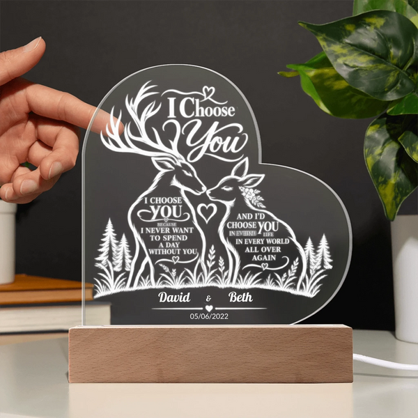 Personalized acrylic LED night light with deer and forest design, held by a hand on a wooden base with a dark background and green plant leaves.