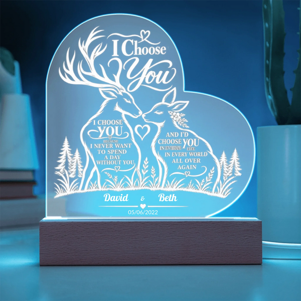 Personalized LED acrylic night light with a heart-shaped glowing panel featuring two deer, floral details, and engraved wedding text on a wooden base, shown in a softly lit room setting.