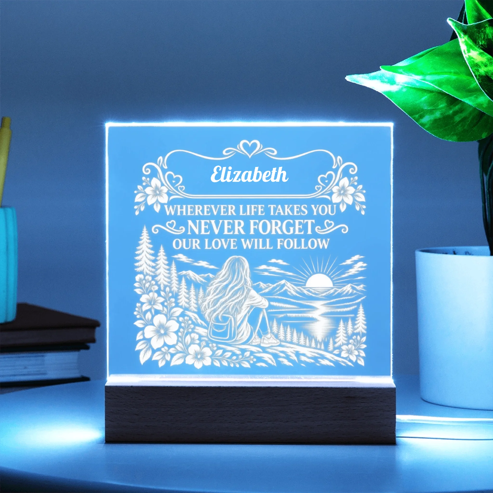 A personalized acrylic LED night light on a dark wooden base, glowing with a blue light. The light features an engraved design of a woman camping by a lake with mountains and flowers, with the name 'Elizabeth' and a memorial quote.