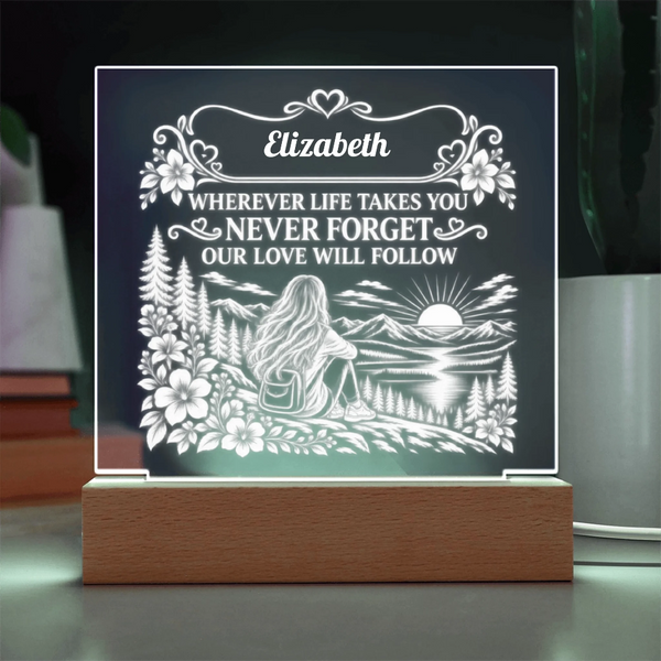 A personalized acrylic LED night light on a wooden base, featuring a white engraved design of a woman sitting by a lake with mountains and flowers, with the text 'Elizabeth WHEREVER LIFE TAKES YOU NEVER FORGET OUR LOVE WILL FOLLOW'.