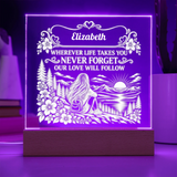 A square acrylic LED night light on a wooden base, glowing with purple light and featuring a custom engraved design with the name 'Elizabeth' and a scenic landscape illustration.