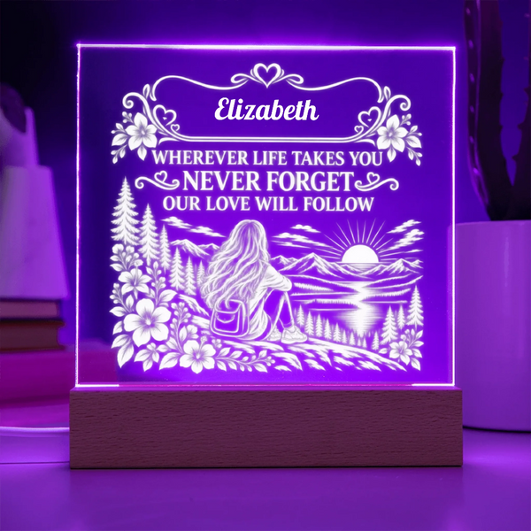 A square acrylic LED night light on a wooden base, glowing with purple light and featuring a custom engraved design with the name 'Elizabeth' and a scenic landscape illustration.