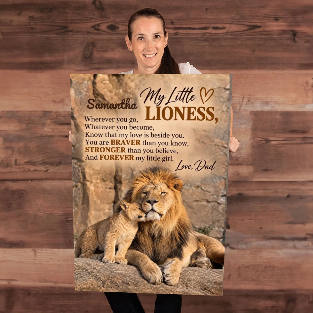 A woman holding a large printed poster or canvas featuring a lion and cub with the text 'My Little Lioness, Love, Dad' and a memorial-style poem, shown against a rustic wood plank background.
