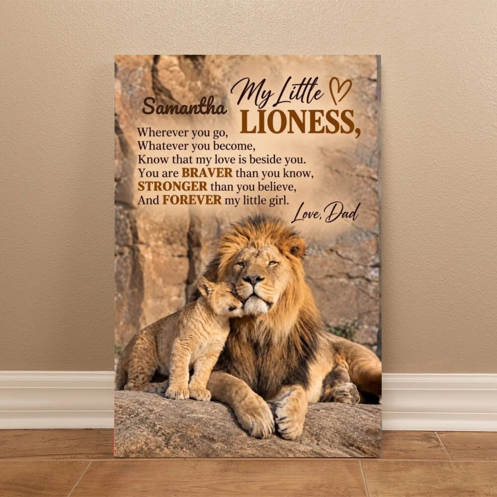 A vertical canvas print leaning against a beige wall on a wood floor, featuring a lion and cub with printed memorial-style text reading 'My Little Lioness, Love, Dad' and a poem about a lioness.
