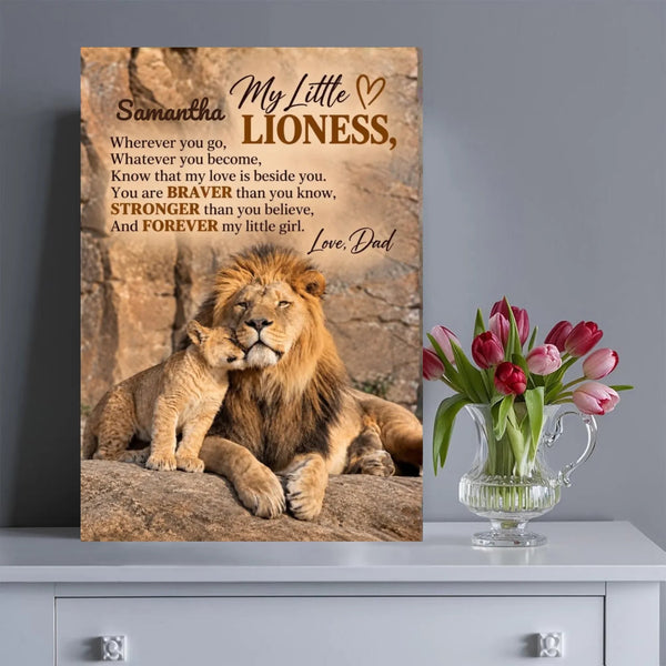 A vertical canvas print featuring a lion and cub with a poem titled 'My Little Lioness' displayed on a gray wall above a white dresser, next to a glass vase of pink tulips.