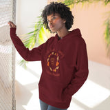 Woman wearing a maroon hoodie with text and graphics, standing indoors with plants in the background