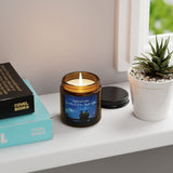 Candle in a glass jar with a label, books, and a plant on a surface.
