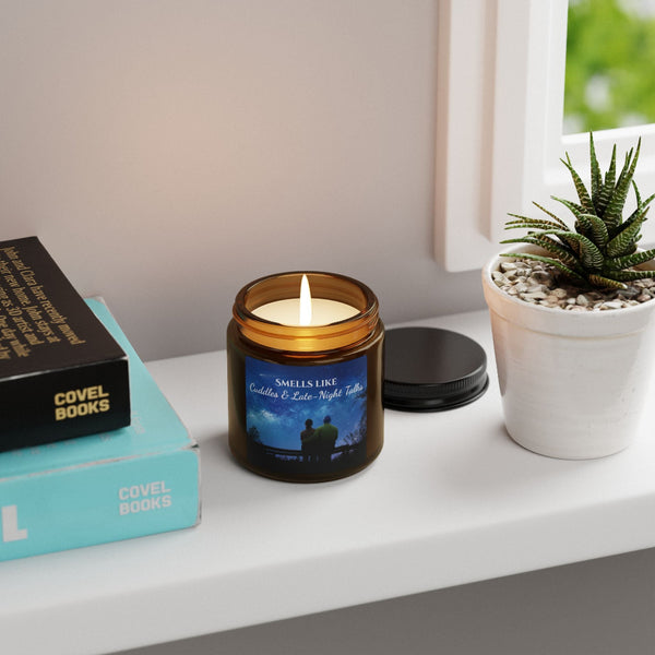 Candle in a glass jar with a label, books, and a plant on a surface.