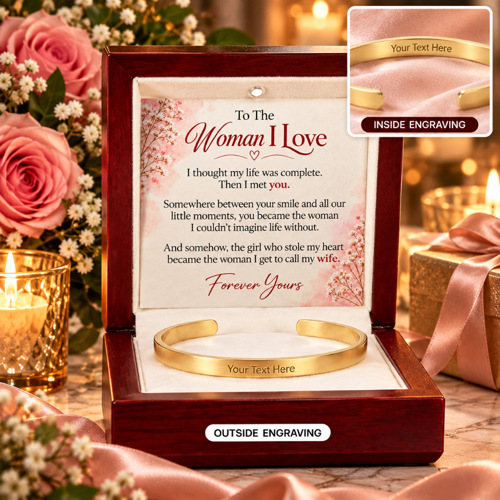 A gold cuff bracelet presented in an open dark wood gift box with a sentimental message card inside. The box is styled with pink roses, lit candles, and satin ribbon.