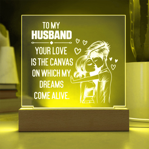 A wooden LED acrylic night light with a glowing yellow-green ambiance, featuring a white laser-engraved illustration of a couple hugging and the text 'TO MY HUSBAND YOUR LOVE IS THE CANVAS ON WHICH MY DREAMS COME ALIVE.'.