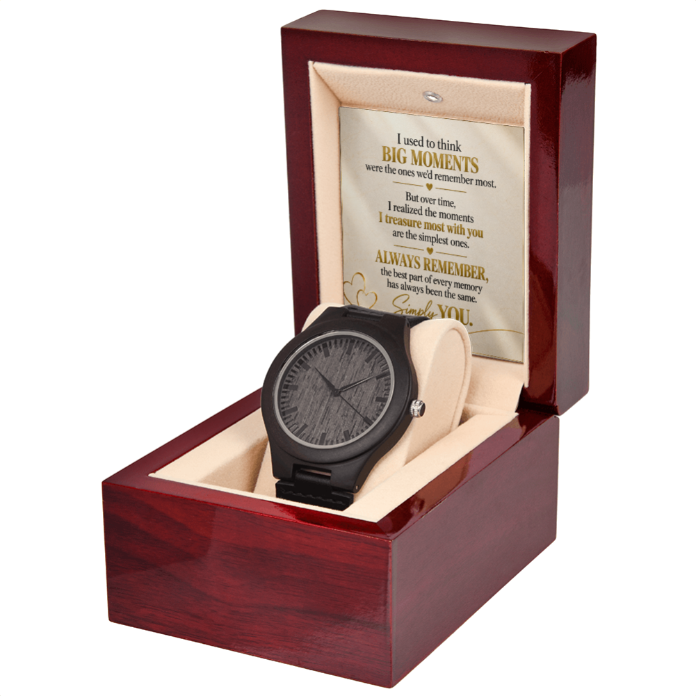 A black wood-grain watch with a black strap is displayed inside an open reddish-brown wooden gift box with a cream cushion. The inside lid features a sentimental message printed on parchment-style paper.
