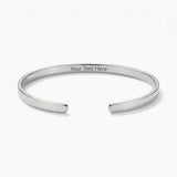 A polished silver-tone open cuff bangle bracelet with 'Your Text Here' engraved on the inside, displayed on a clean white background.