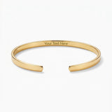 A polished gold-tone open cuff bangle bracelet with 'Your Text Here' engraved on the inside, displayed on a clean white background.