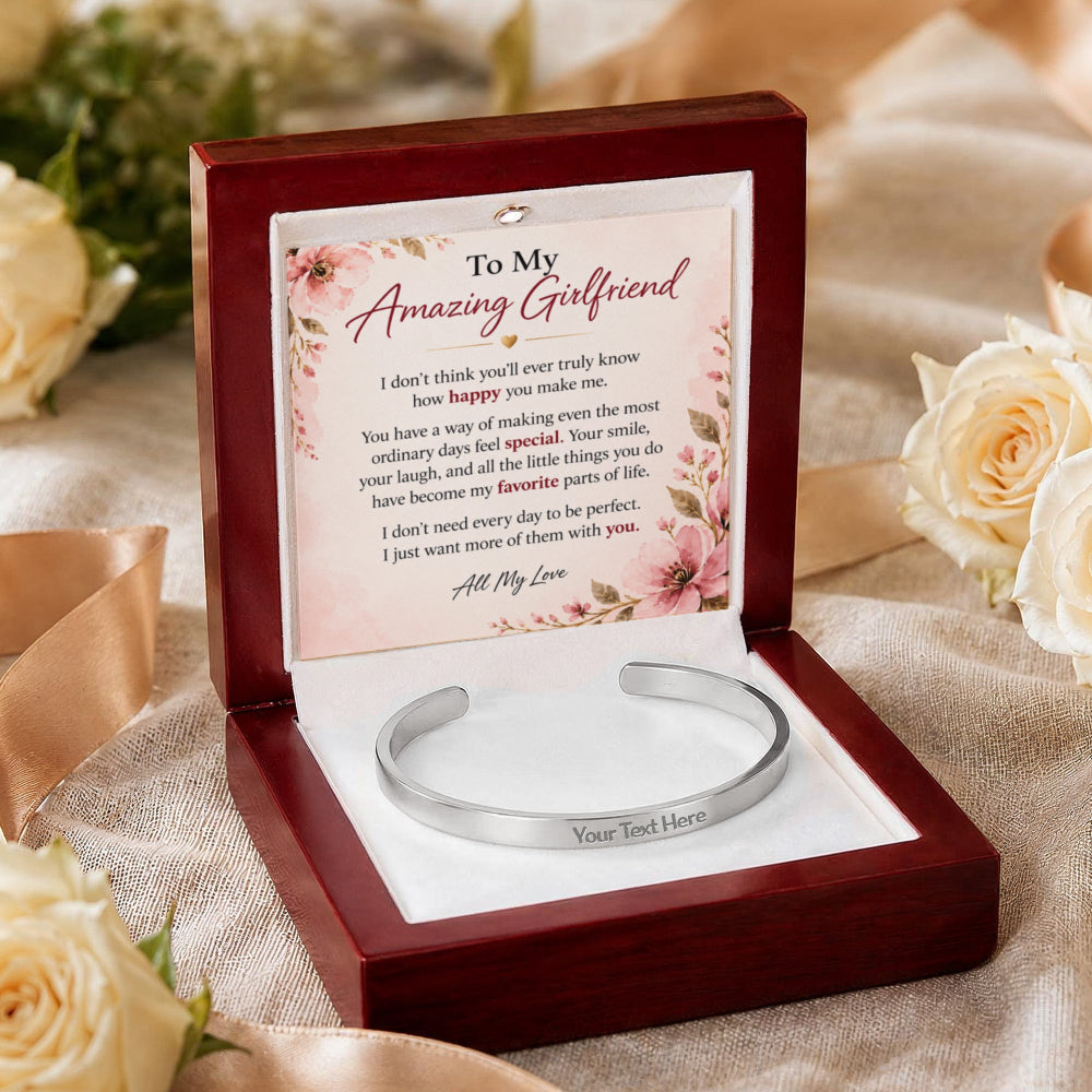 A personalized silver cuff bracelet presented in an open dark wood gift box with a floral message card. The card reads 'To My Amazing Girlfriend' and includes a placeholder for the friend's name.