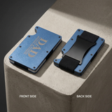 A slim blue metal card holder wallet shown from both front and back sides on a white background. The front side features a textured blue finish with a debossed gold 'DAD' design, while the back side shows a black plastic buckle and a black hook-and-loop strap.