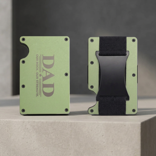 A split view of a slim metal wallet shown from the front and back on a white background. The front side is light olive green with dark gray text reading 'DAD OUR ROCK OUR STRENGTH.
