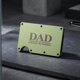 A slim, rectangular metal wallet in a muted sage green color, featuring the text 'DAD OUR ROCK. OUR STRENGTH.