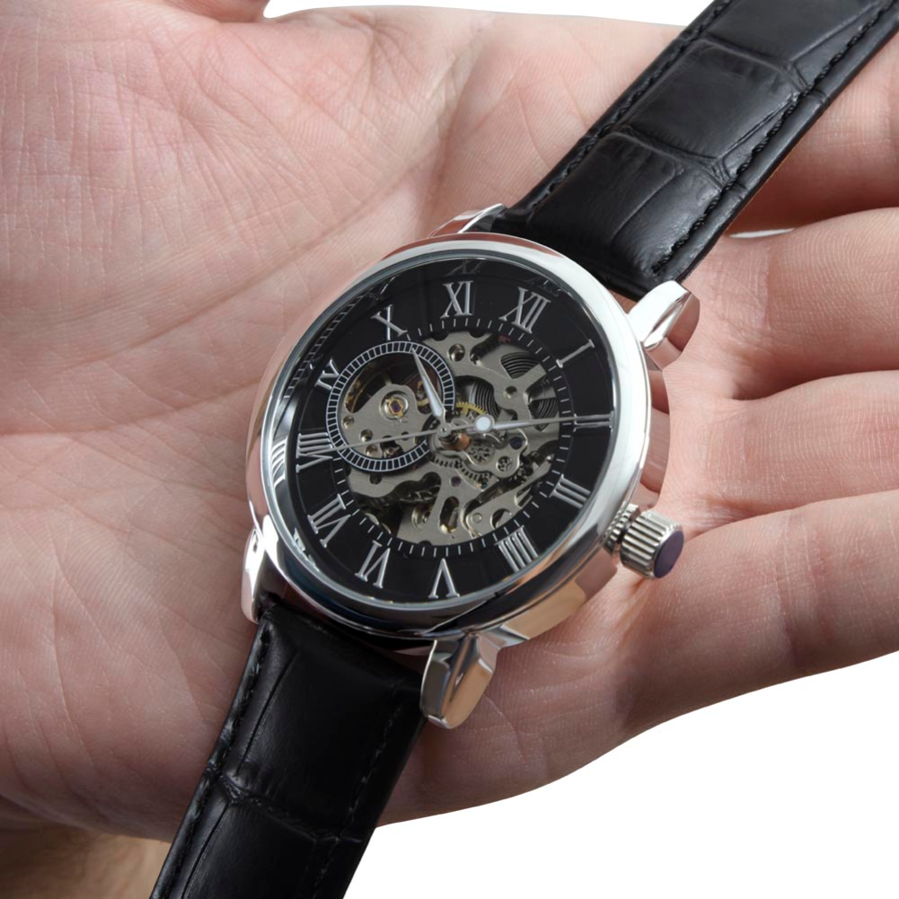 Close-up of a men's automatic skeleton watch with black leather strap and exposed mechanical dial held in a hand.