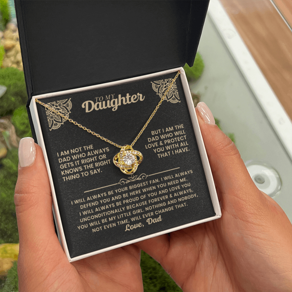 A person holds an open black gift box containing a gold necklace with a clear rhinestone clover pendant, displayed over a printed sentimental message card addressed 'To My Daughter'.