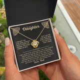 A person holds an open black gift box containing a gold necklace with a clear rhinestone clover pendant, displayed over a printed sentimental message card addressed 'To My Daughter'.