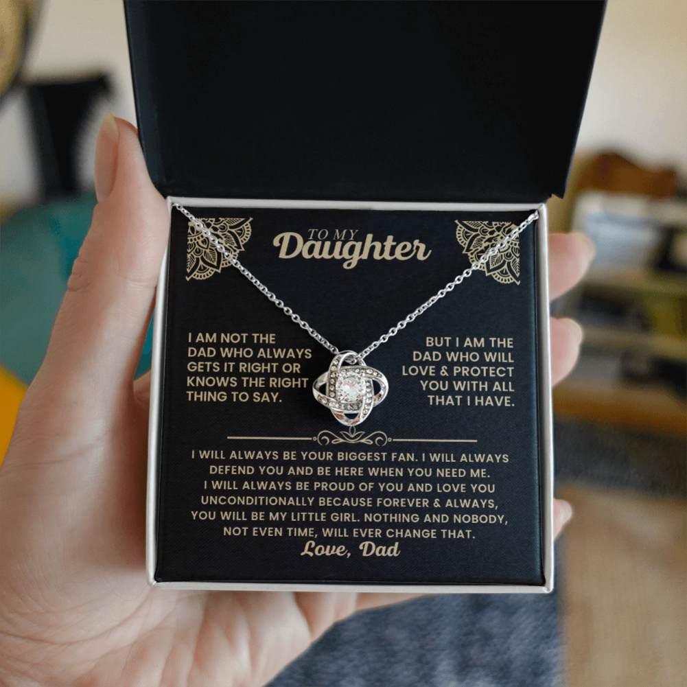 A hand holds an open black jewelry gift box containing a silver chain necklace with a clear crystal pendant, displayed on a black printed message card with German text.