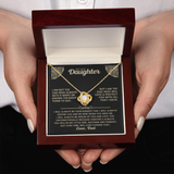 A person holding an open dark wood gift box containing a gold necklace with a heart-shaped pendant and a printed message card addressed to a wife.