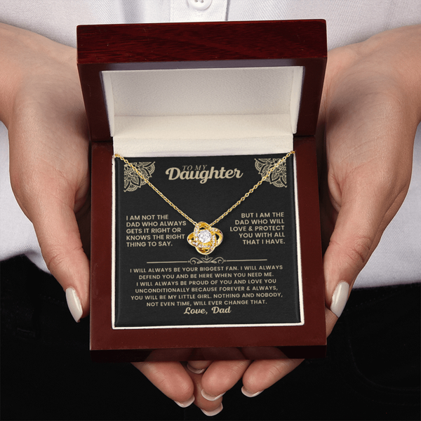 A person holding an open dark wood gift box containing a gold necklace with a heart-shaped pendant and a printed message card addressed to a wife.