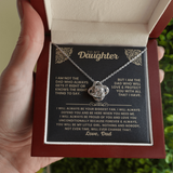 A hand holding an open burgundy gift box containing a necklace presented on a black card with gold text and floral corner designs. The necklace has a silver-toned chain and a rose-shaped pendant.