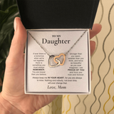 A hand holds an open jewelry gift box containing a necklace with two interlocking heart pendants in silver and gold tones, displayed on a printed message card addressed 'TO MY Daughter'.