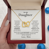 A gold heart-link necklace displayed on a printed message card inside a red gift box, held by a hand. The card is addressed 'TO MY Daughter' with a sentimental message, and the necklace features two interlocking gold hearts.