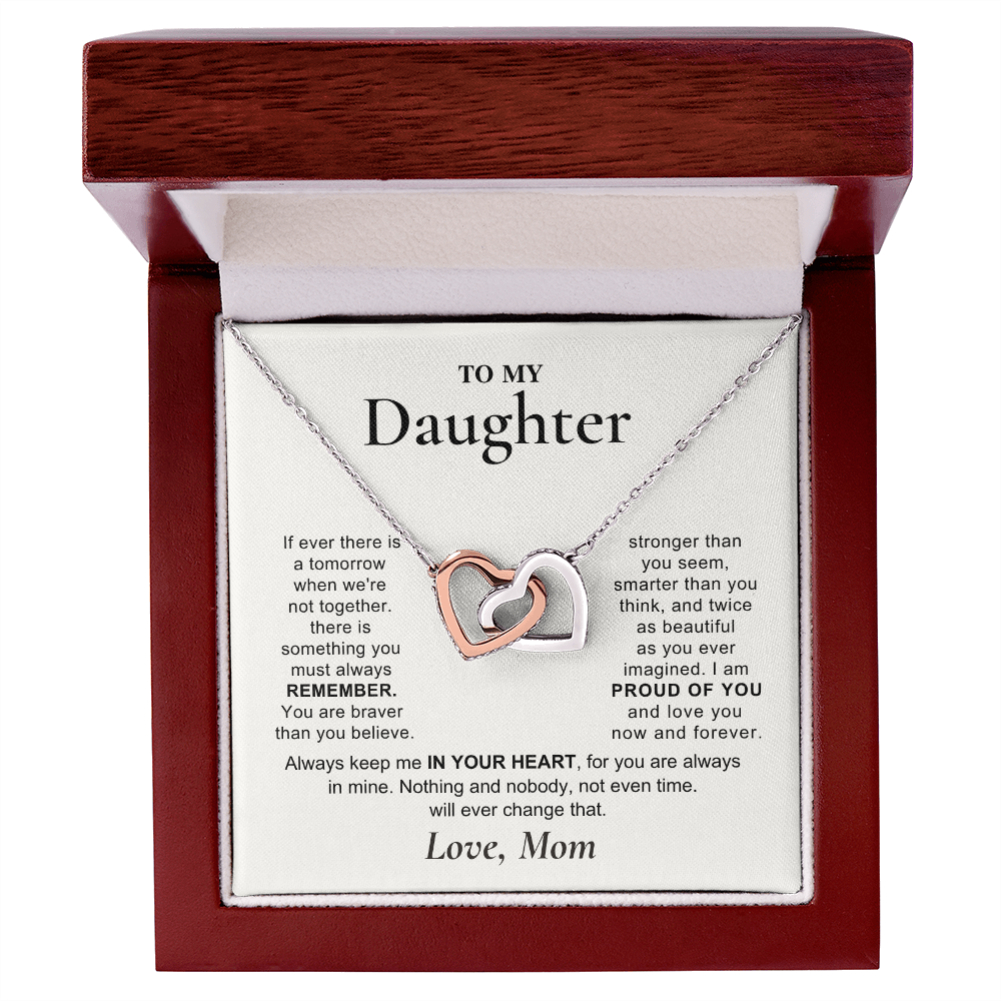 A heart-shaped pendant necklace with one silver heart and one rose gold heart, presented in an open dark wood gift box with a sentimental message card addressed to 'My Daughter'.