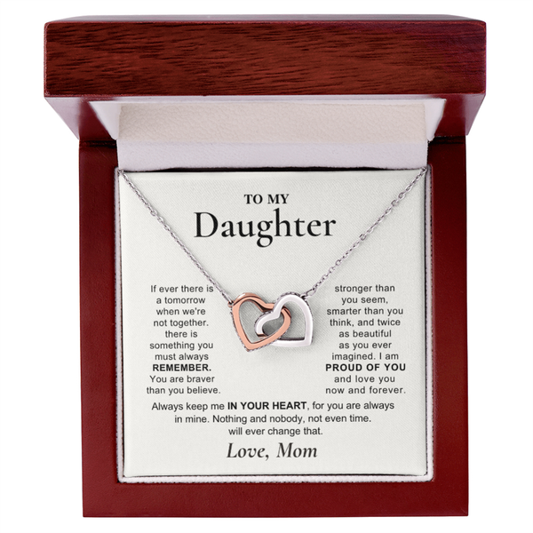 A heart-shaped pendant necklace with one silver heart and one rose gold heart, presented in an open dark wood gift box with a sentimental message card addressed to 'My Daughter'.
