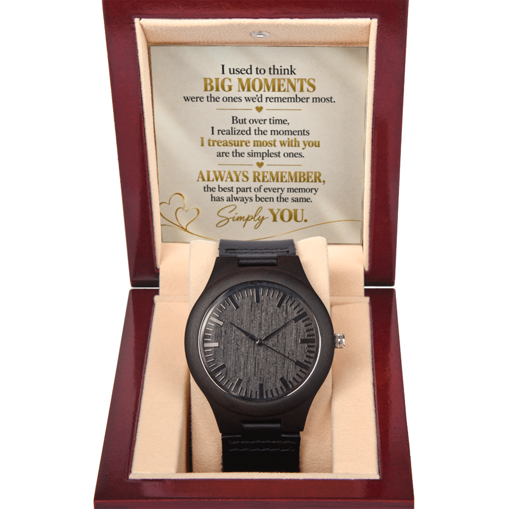 A black wooden wristwatch with a textured wood grain dial and black strap, presented inside an open dark red wooden gift box with a beige cushion. The inside lid features a sentimental message printed in gold and black text.