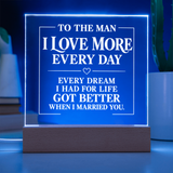 A rectangular acrylic LED sign on a wooden base glowing with blue light, featuring white text that reads, 'TO THE MAN I LOVE MORE EVERY DAY EVERY DREAM I HAD FOR LIFE GOT BETTER WHEN I MARRIED YOU.'.