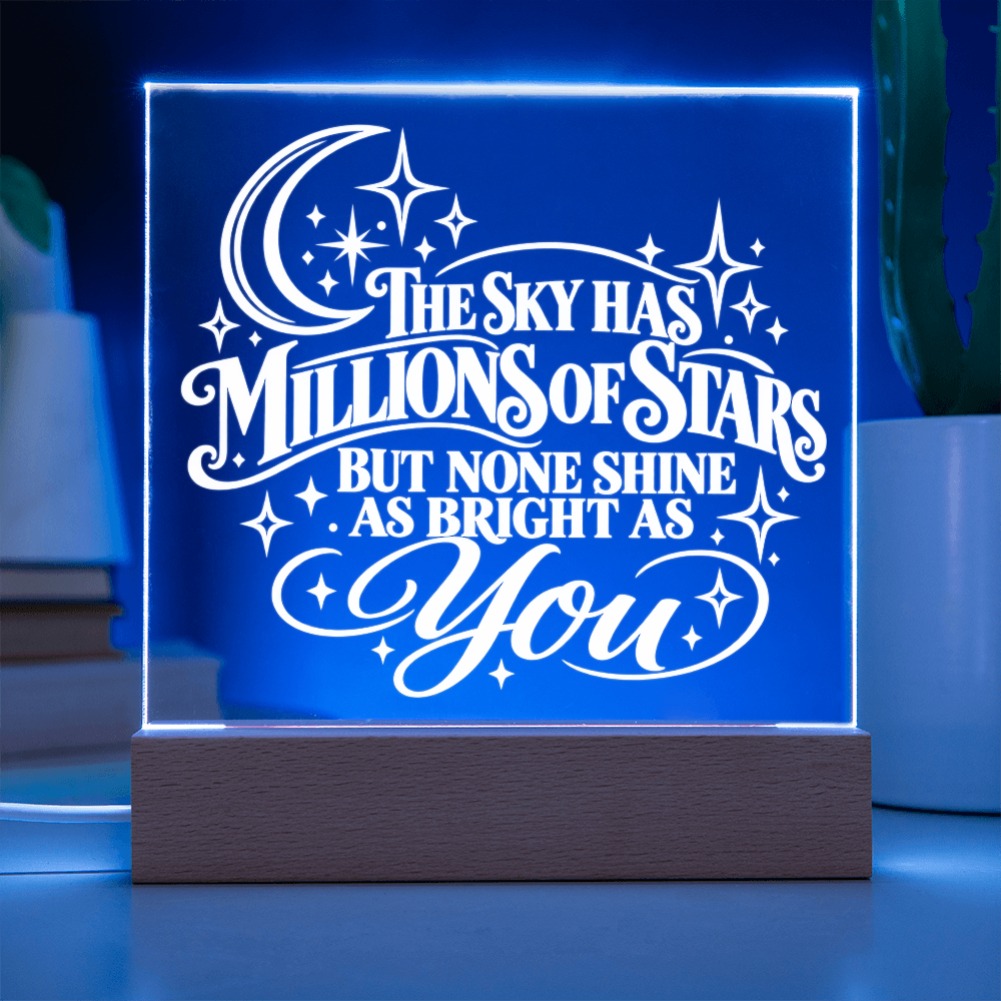 A glowing acrylic LED night light on a wooden base, displaying the quote 'THE SKY HAS MILLIONS OF STARS BUT NONE SHINE AS BRIGHT AS You' in white against a blue illuminated background.