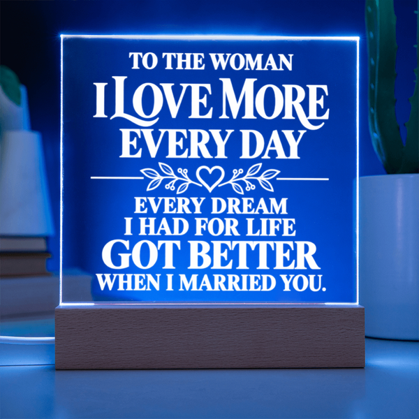 A rectangular LED acrylic lamp on a wooden base, glowing with a blue light and featuring white engraved text that reads, 'TO THE WOMAN I LOVE MORE EVERY DAY EVERY DREAM I HAD FOR LIFE GOT BETTER WHEN I MARRIED YOU.'.