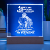 A rectangular acrylic LED lamp on a wooden base, glowing blue with white engraved text and a couple illustration. The text reads, '4 BILLION MEN, 195 COUNTRIES, 7,000+ LANGUAGES.