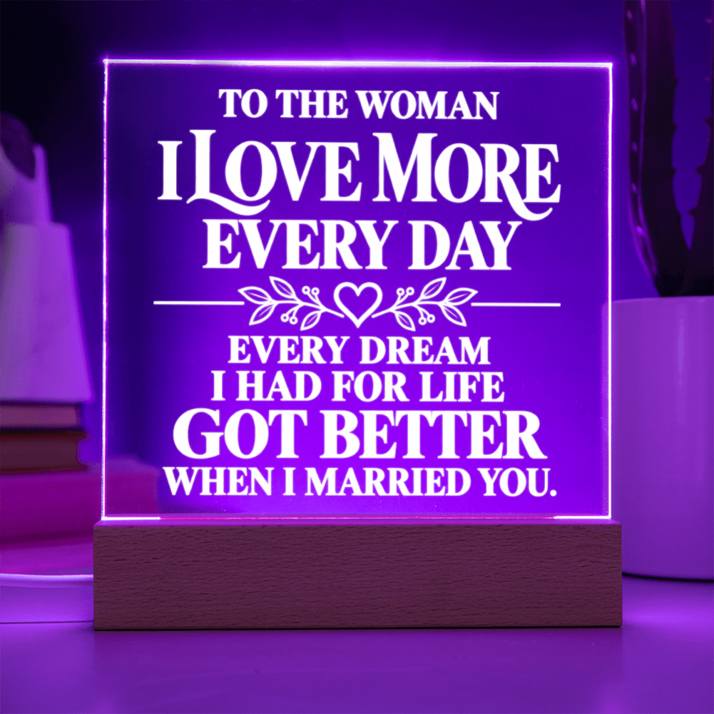 A rectangular LED acrylic lamp on a wooden base, glowing with purple light and featuring white text that reads, 'TO THE WOMAN I LOVE MORE EVERY DAY EVERY DREAM I HAD FOR LIFE GOT BETTER WHEN I MARRIED YOU.'.