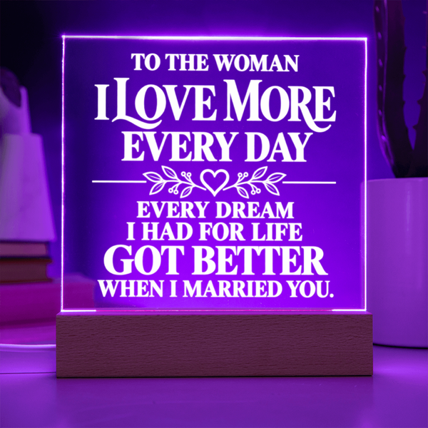 A rectangular LED acrylic lamp on a wooden base, glowing with purple light and featuring white text that reads, 'TO THE WOMAN I LOVE MORE EVERY DAY EVERY DREAM I HAD FOR LIFE GOT BETTER WHEN I MARRIED YOU.'.
