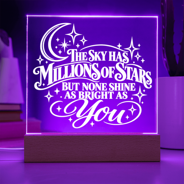 A square acrylic LED night light on a wooden base, glowing with a purple light and featuring the white text 'THE SKY HAS MILLIONS OF STARS BUT NONE SHINE AS BRIGHT AS You' with a crescent moon and stars.